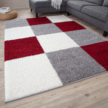 Load image into Gallery viewer, A shaggy area rug with a geometric pattern of squares in gray, white, and red colors, placed on a wooden floor.