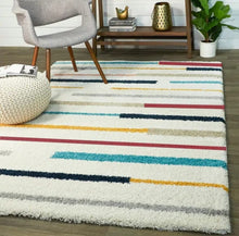 Load image into Gallery viewer, Multicolored striped rug on a wooden floor with a chair and ottoman in the background.