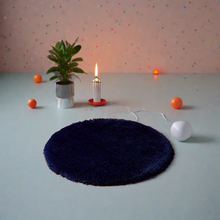 Load image into Gallery viewer, A round, blue shaggy rug is displayed on a light background with a decorative candle, an orange plant, and a red dish with a white ball next to it.