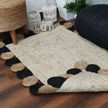 Load image into Gallery viewer, Woven rug with black and beige circular patterns on a wooden floor.