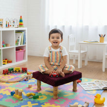Load image into Gallery viewer, Child sitting on a small stool in a playroom with toys and books around