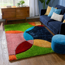 Load image into Gallery viewer, A multi-colored shaggy area rug with abstract geometric patterns placed on a floor in a room with a blue sofa, wooden cabinet, and decorative pillows.
