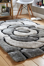 Load image into Gallery viewer, A modern shaggy rug with a gray rose pattern, placed on a wooden floor in a well-lit living room setting with a chair, plant, and books in the background.