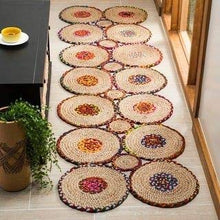 Load image into Gallery viewer, A series of round braided natural jute rugs with colorful cotton stripes, placed on the floor in a home setting, with a plant and a round decorative object in the background.