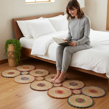 Load image into Gallery viewer, Woman sitting on a bed reading a book with decorative coasters on the floor.
