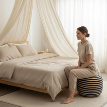 Load image into Gallery viewer, Woman sitting on a striped ball next to a bed in a softly lit bedroom.
